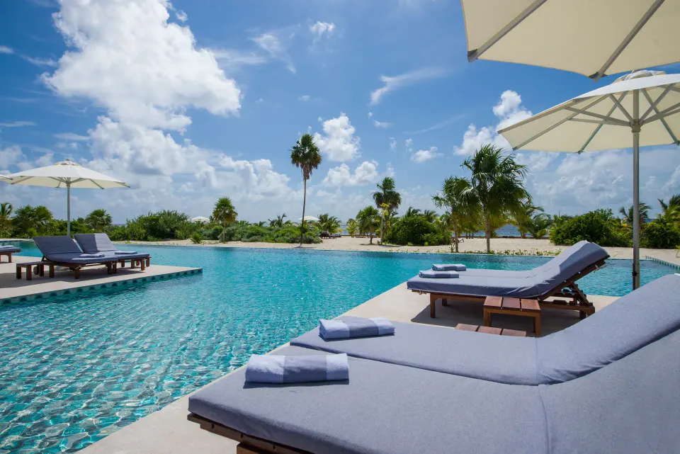 Pool loungers with towels under white umbrellas at Chablé Maroma.