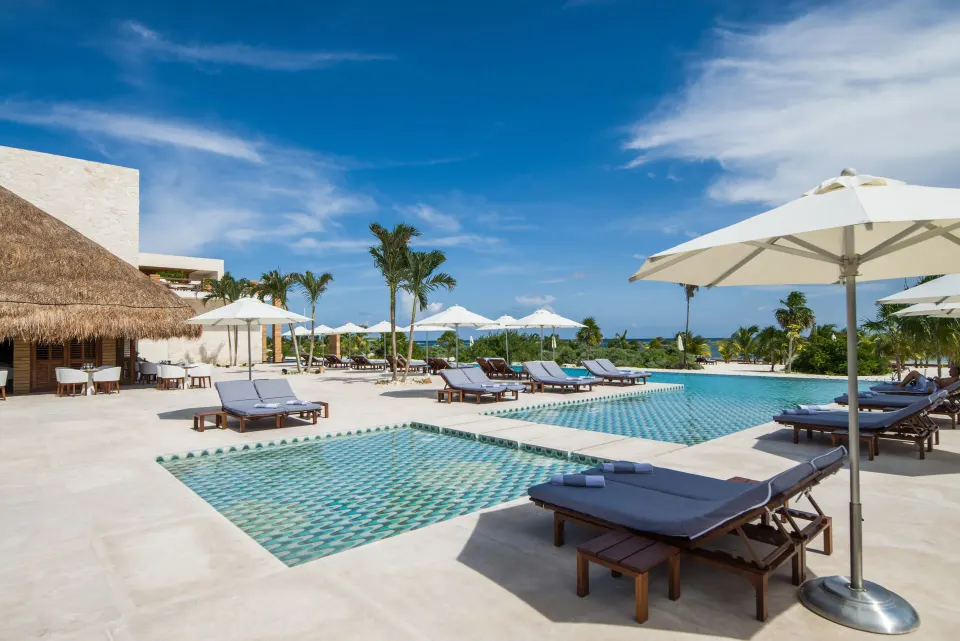 Pool terrace with loungers, white umbrellas, palms, and ocean beyond at Chablé Maroma.