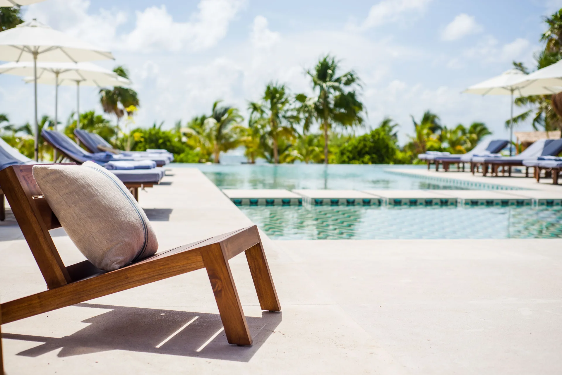Poolside lounge chair with umbrellas and palms at Chablé Maroma.