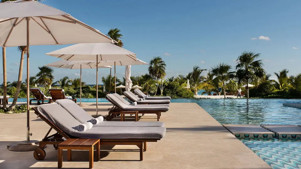 Poolside loungers and white umbrellas beside the water at Chablé Maroma.