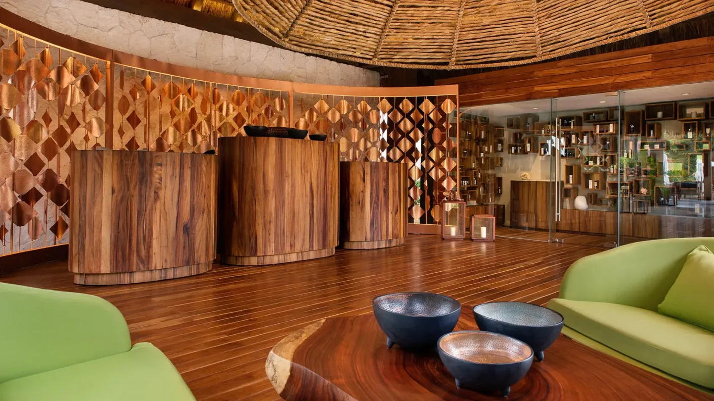 Reception lobby with wood desks, green sofas, and decorative screens at Chablé Maroma.