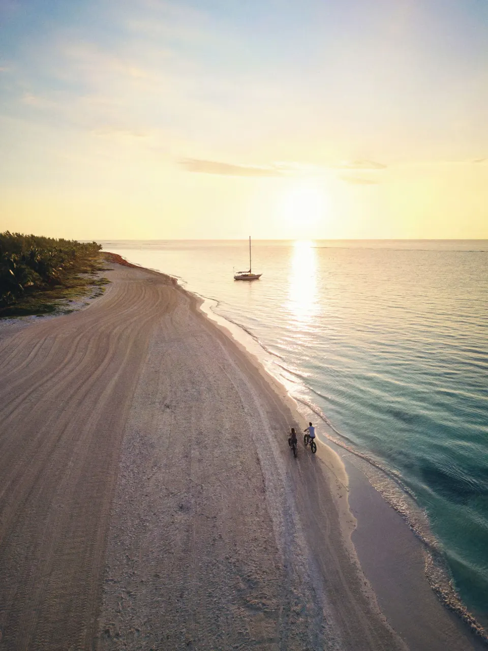 Aerial sunset view of the beach, ocean, sailboat and two cyclists at Chablé Maroma.