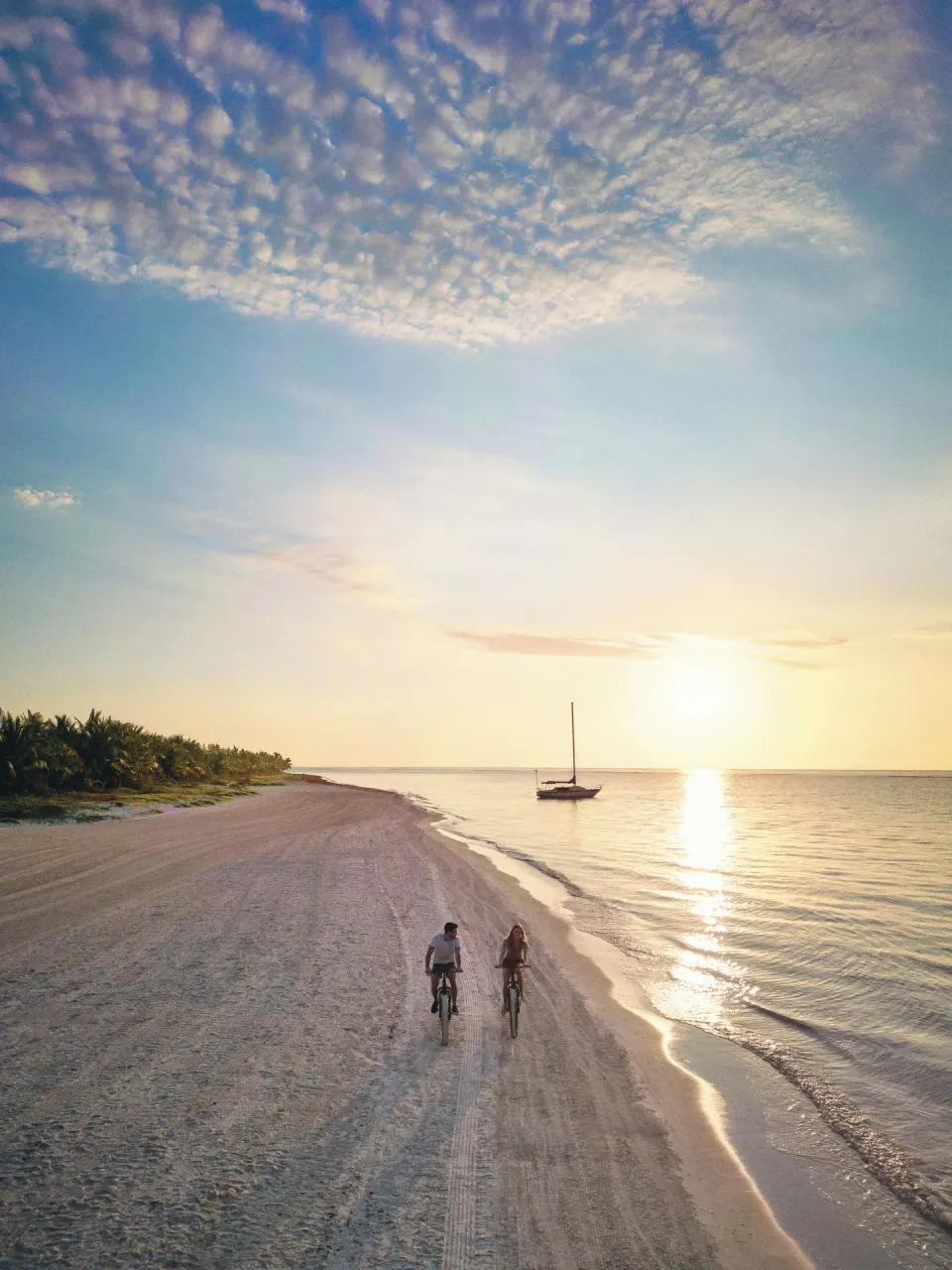 Two cyclists ride along the beach at sunset at Chablé Maroma.