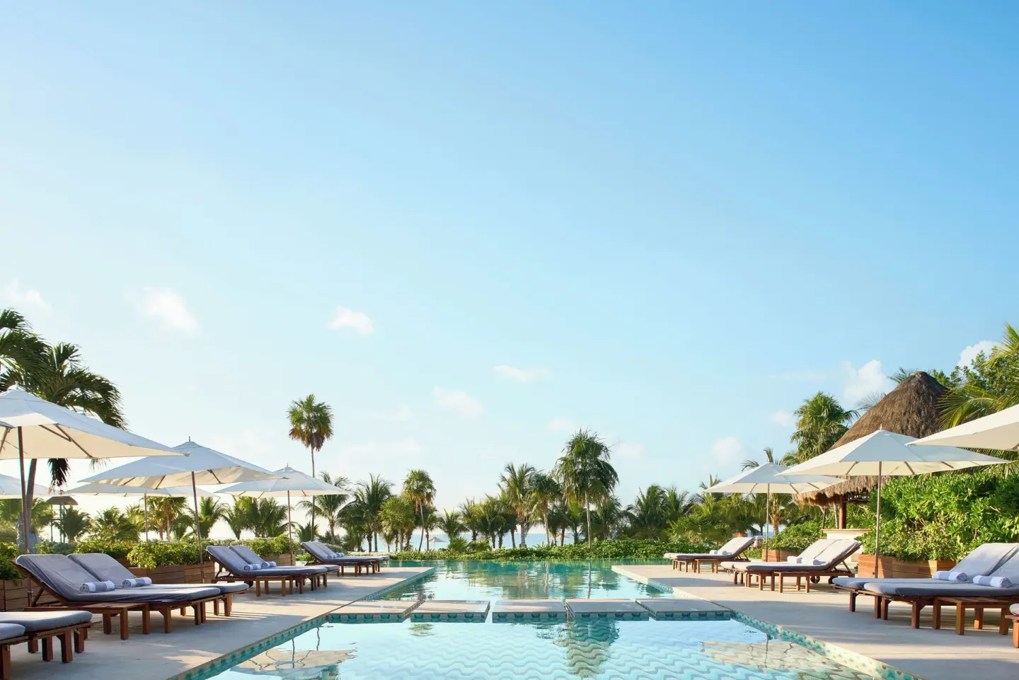 Symmetrical pool deck with loungers, umbrellas, and palms at Chablé Maroma.