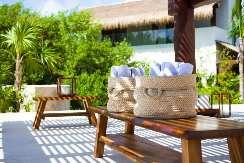 Woven baskets of rolled towels on a bench by the pool at Chablé Maroma