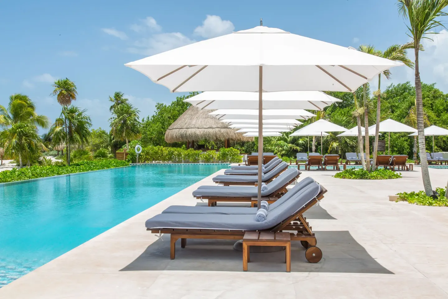 White umbrellas shade gray loungers along the turquoise pool at Chablé Maroma.