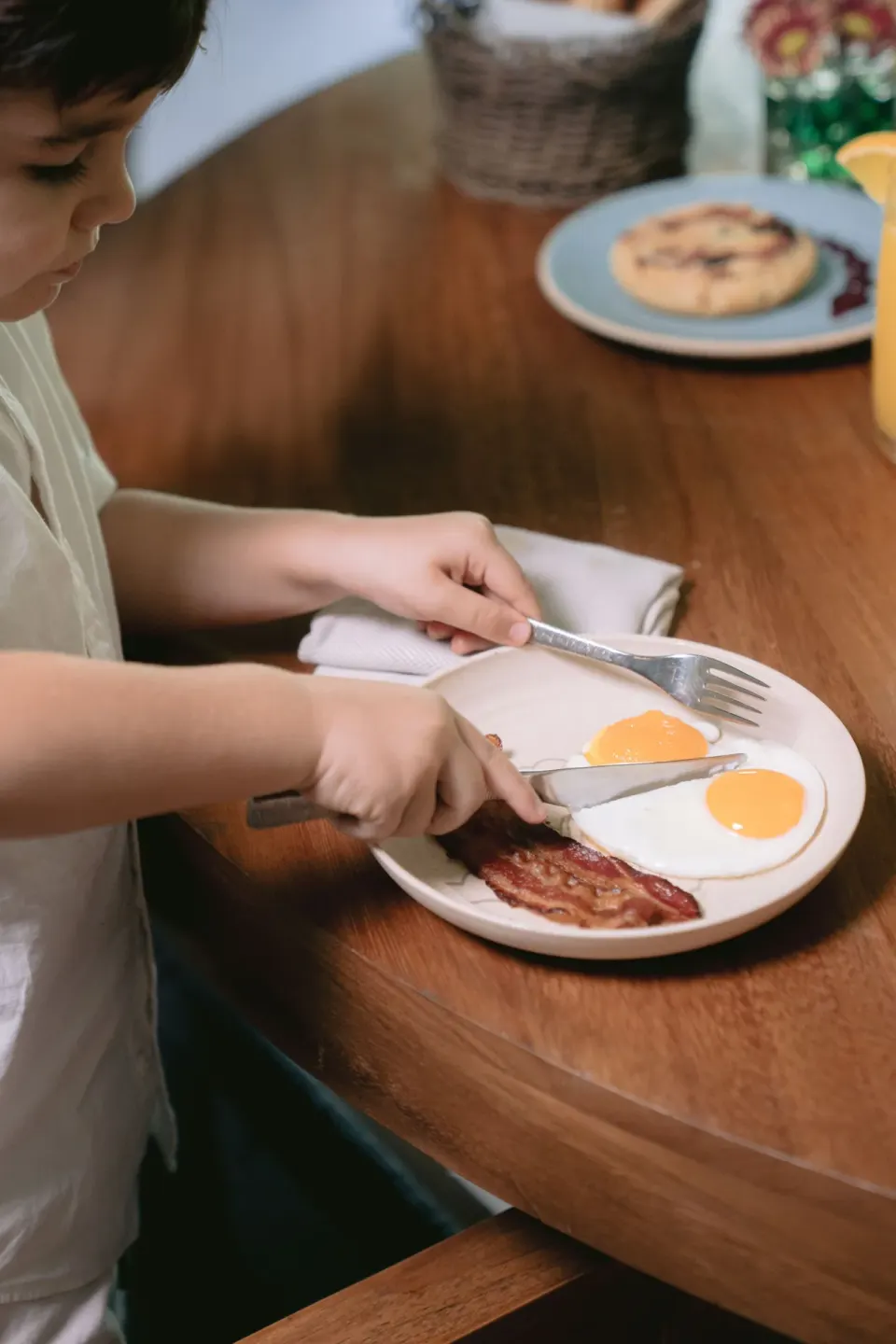 Child cutting eggs and bacon at a breakfast table at Chablé Maroma