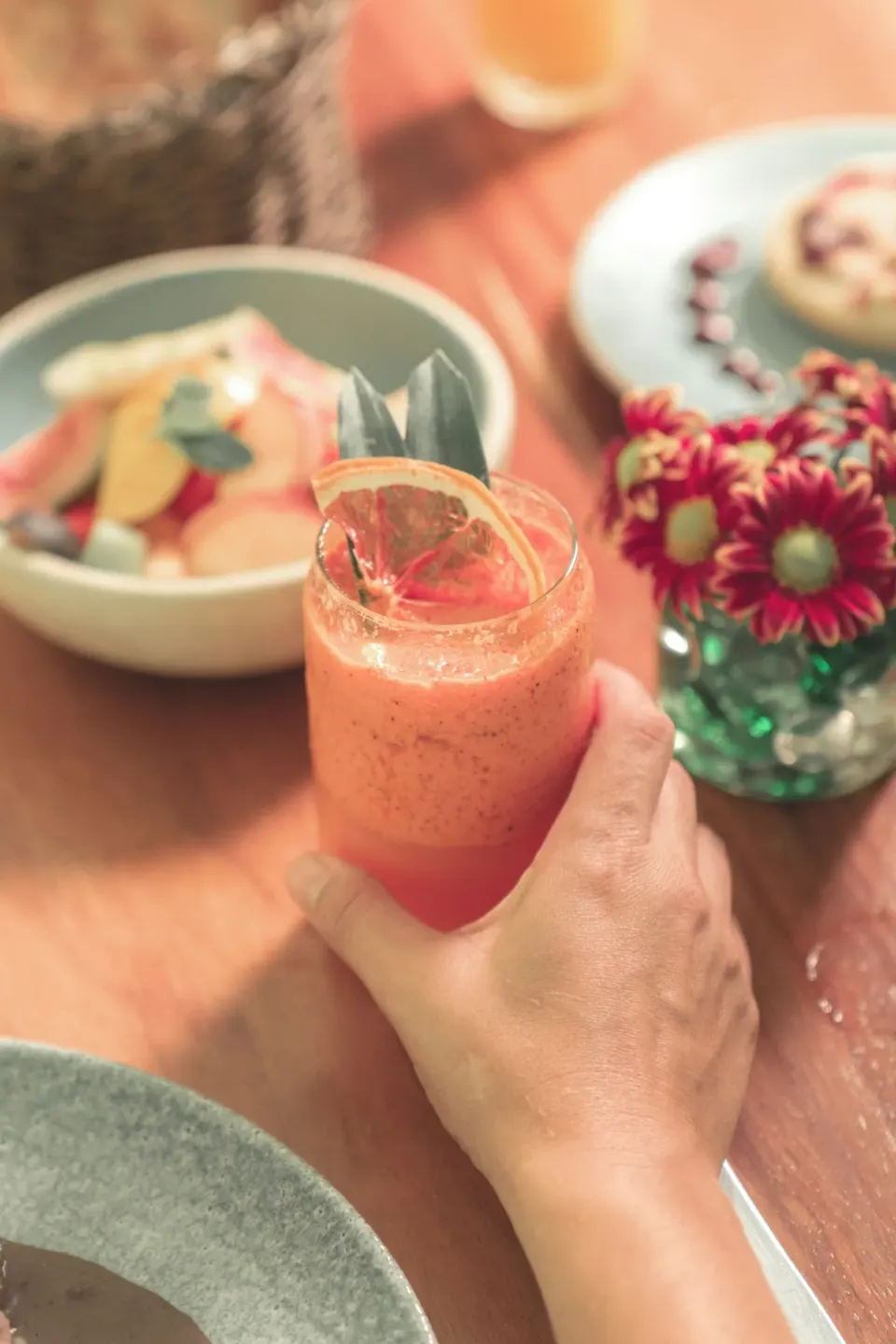 Hand holding a pink smoothie with bowls and flowers on the table at Chablé Maroma