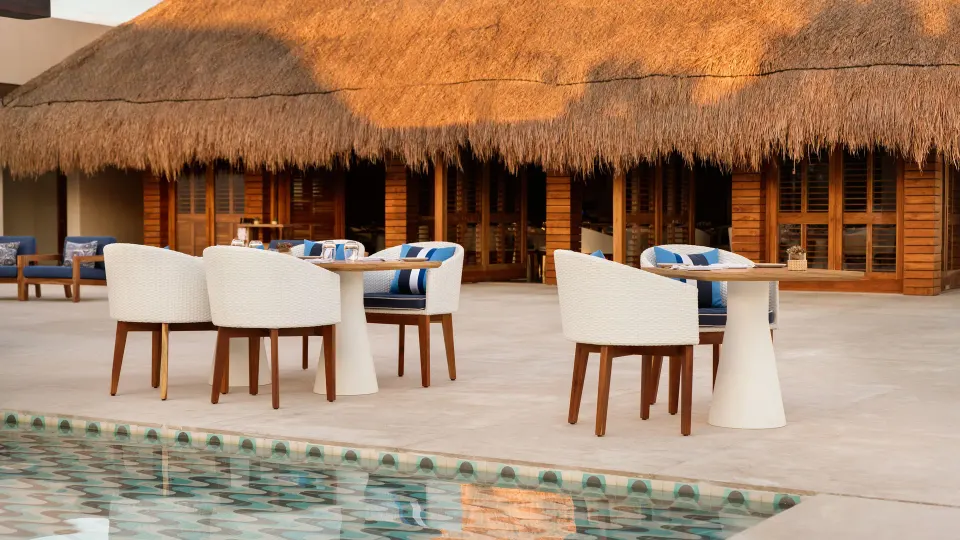 Outdoor dining tables and white chairs by a shallow pool and palapa at Chablé Maroma