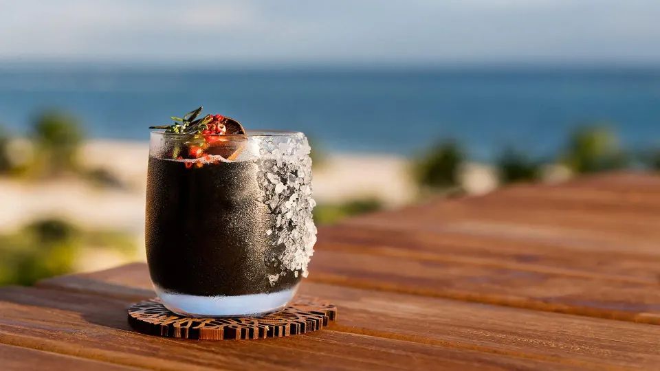 Dark cocktail with salt rim on a table and ocean backdrop at Chablé Maroma
