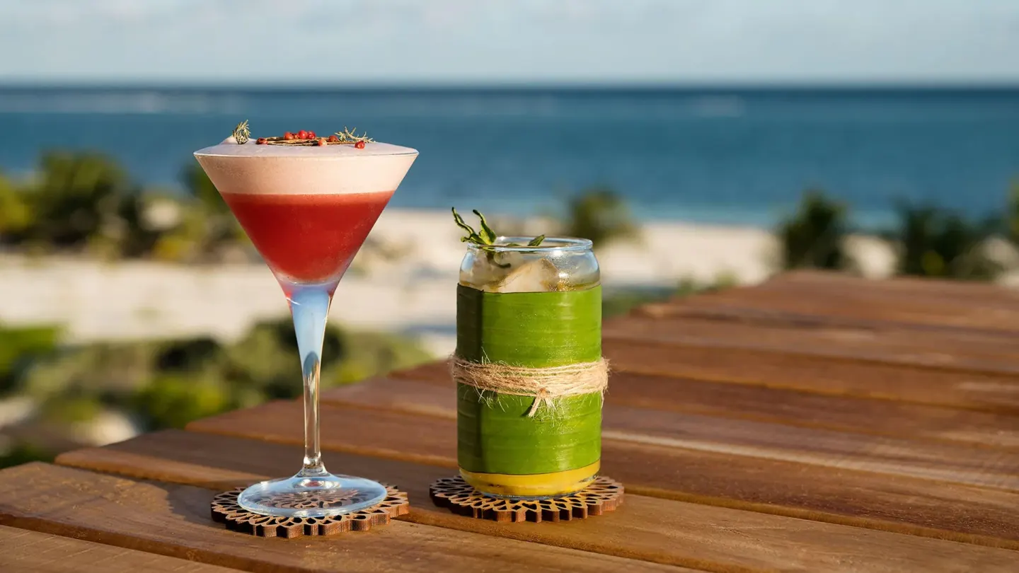 Two colorful cocktails on a wooden table with the sea beyond at Chablé Maroma.