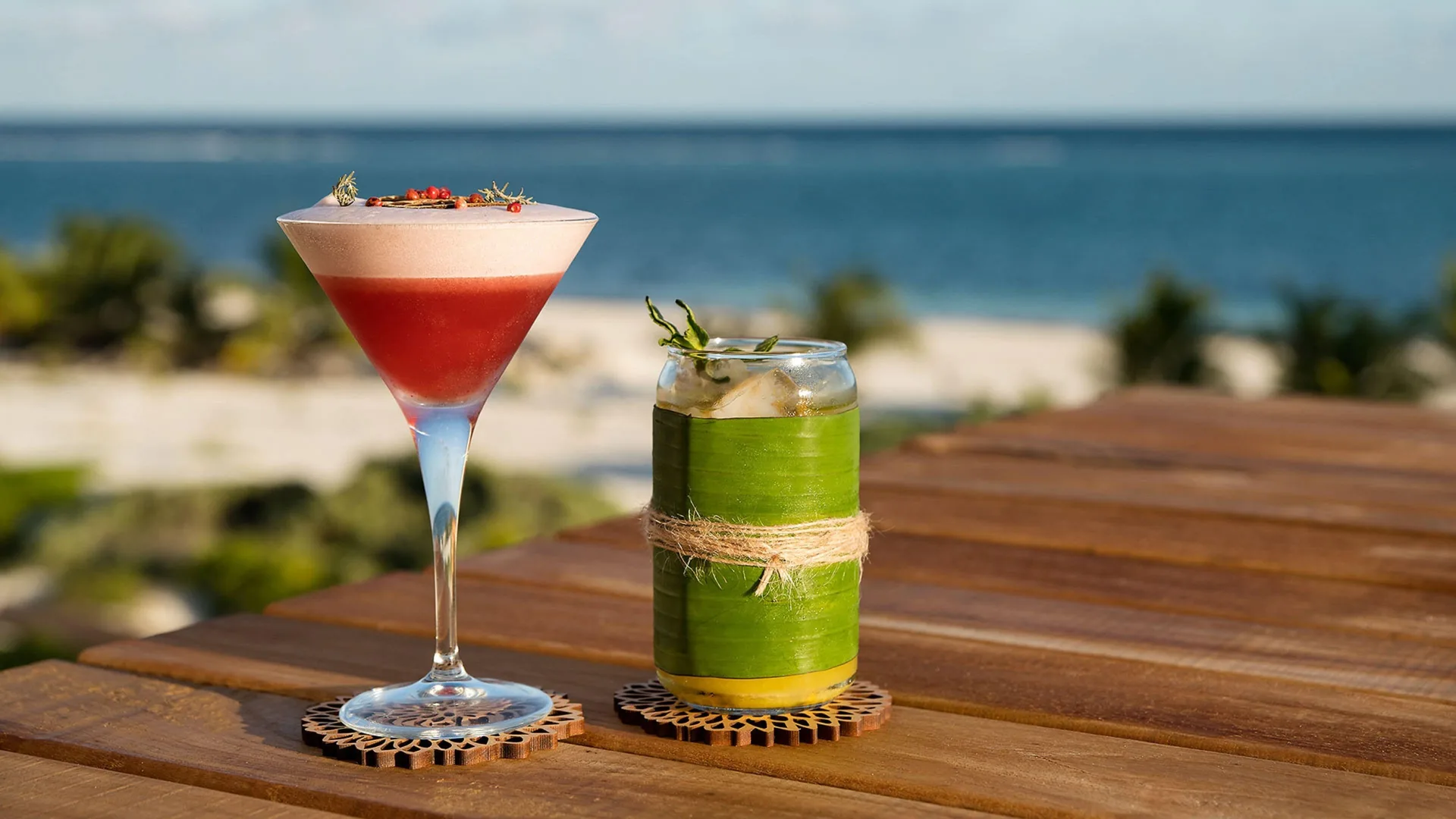 Two colorful cocktails on a wooden table with the sea beyond at Chablé Maroma.
