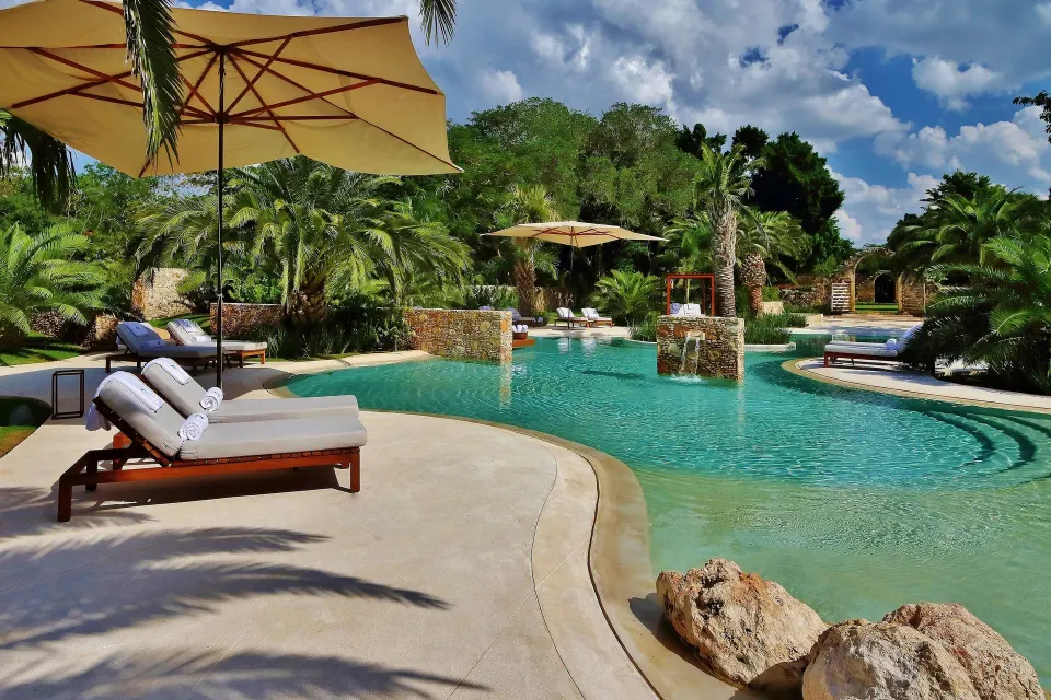 Curved pool edge with loungers and umbrellas in a tropical setting at Chablé Yucatán