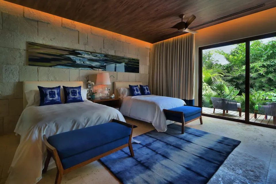 Twin-bedded guest room with blue accents and sliding glass doors at Chablé Yucatán