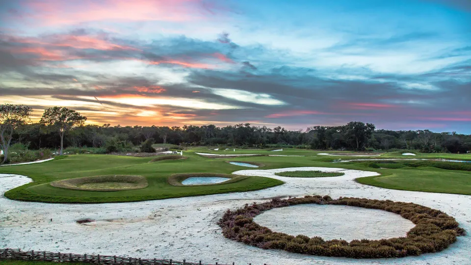 Wide view of manicured golf course fairways and bunkers at Chablé Yucatán at sunset.