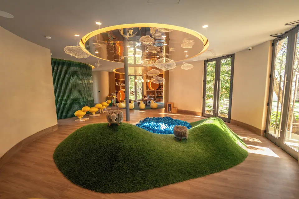 Wide view of the Kids Club playroom with grassy mounds and a central blue pit at Chablé Yucatán.