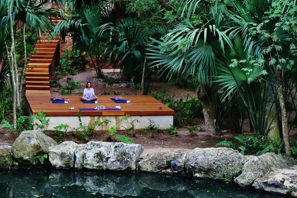 Woman meditating on a wooden deck by a lagoon at Chablé Yucatán
