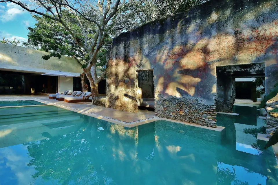 Reflective resort pool with stone wall and shaded cabana at Chablé Yucatán