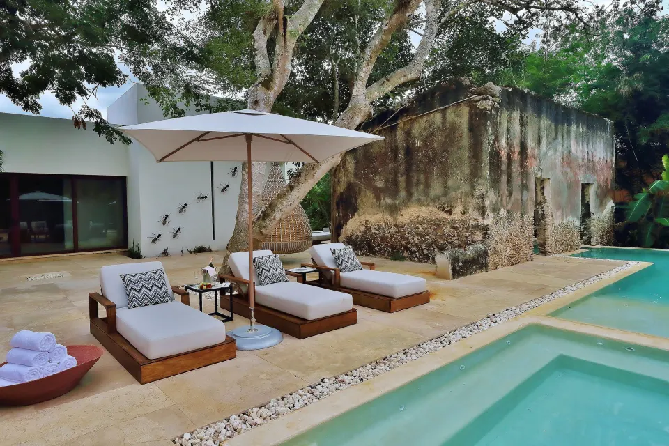 Poolside loungers with umbrella and tree-shaded ruins at Chablé Yucatán