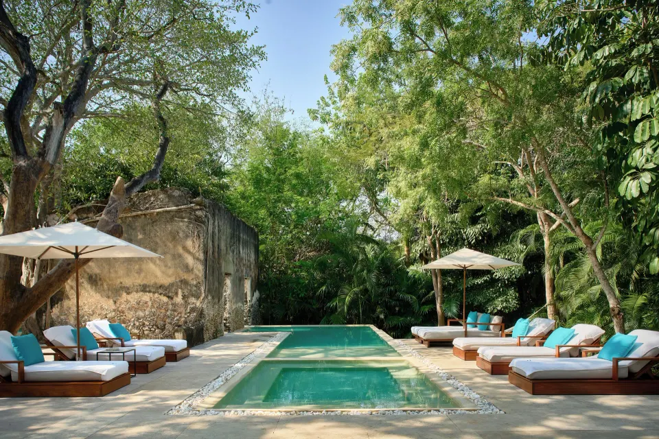 Long rectangular pool with cushioned sun beds and umbrellas at Chablé Yucatán