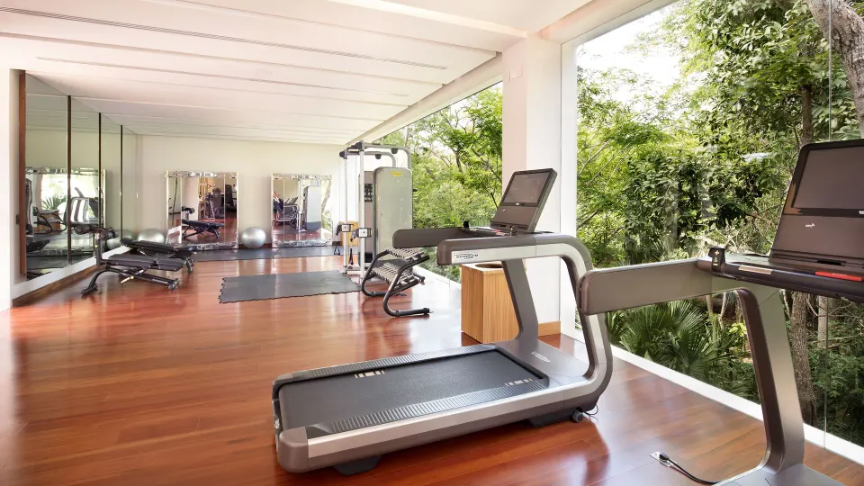 Treadmills and strength equipment beside an open-air window with greenery at Chablé Yucatán