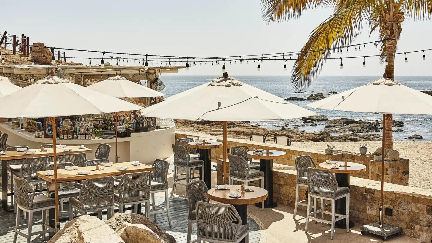 Beachfront terrace with umbrellas and bar seating at Chileno Bay Resort & Residences.