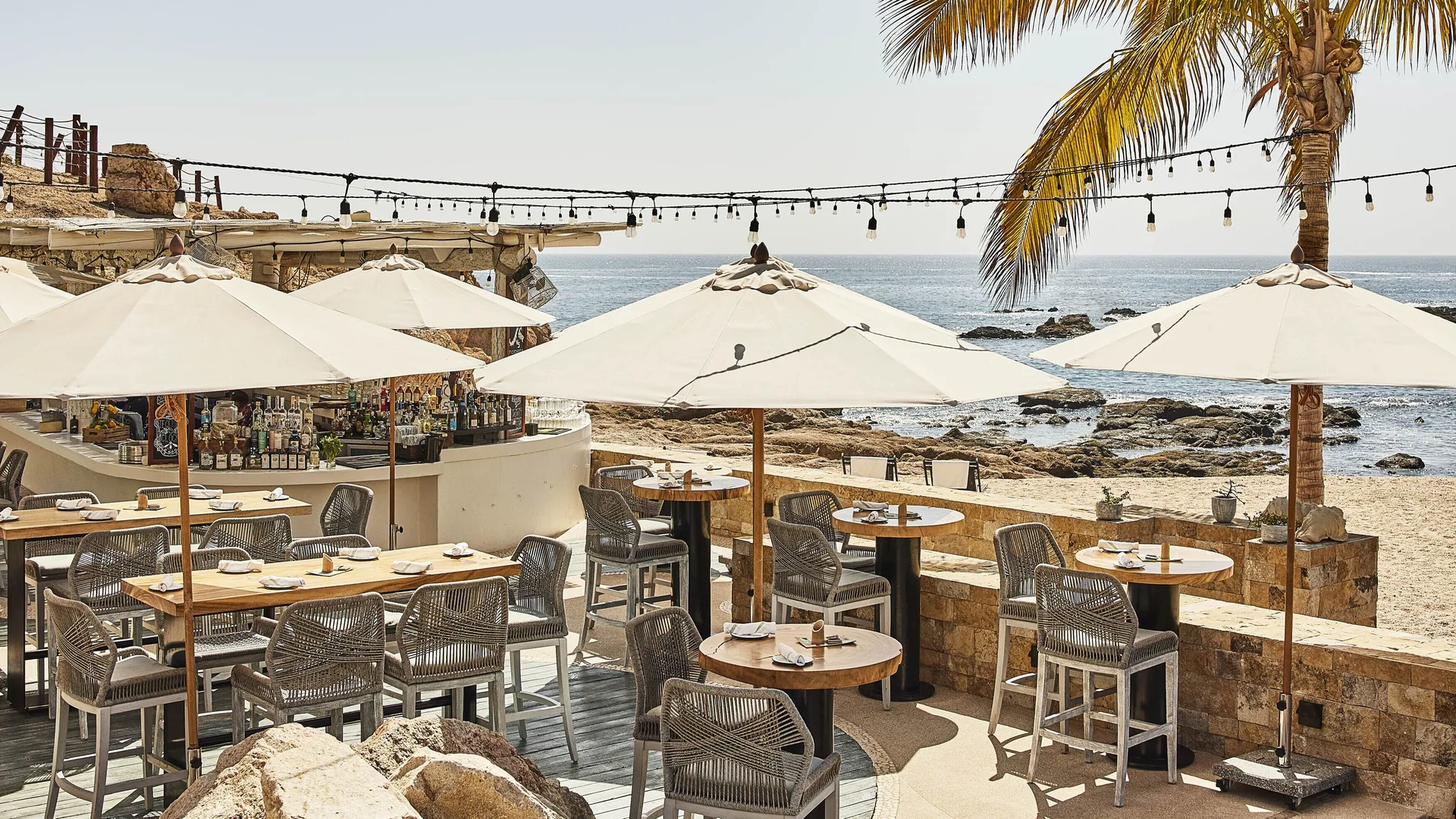 Beachfront terrace with umbrellas and bar seating at Chileno Bay Resort & Residences.
