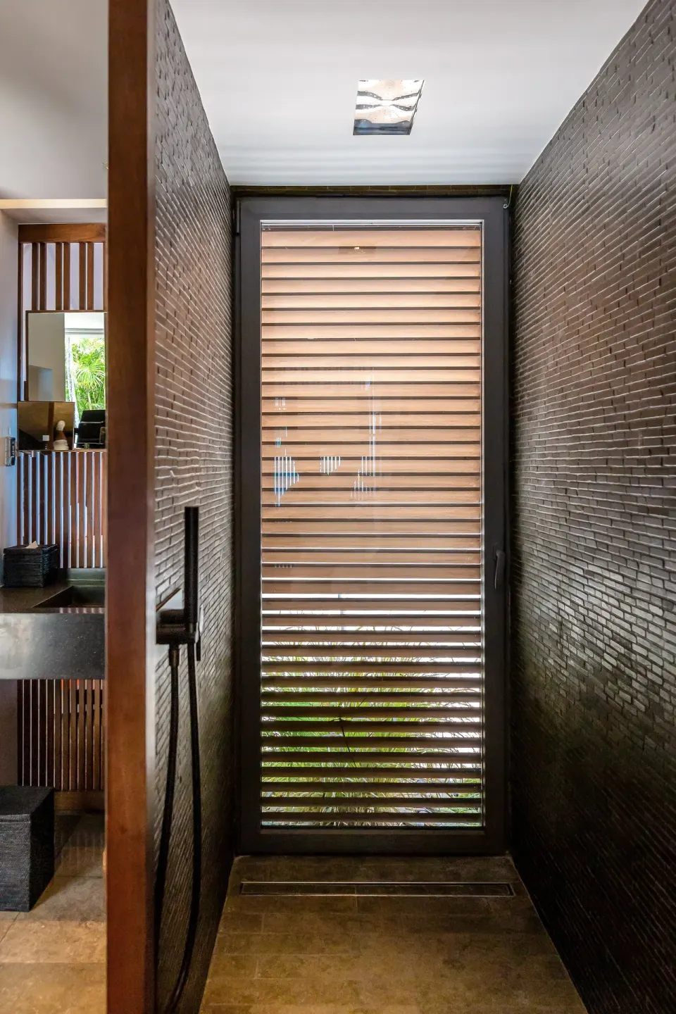Narrow guest room shower area with dark tile and louvered window at Christopher Hotel.