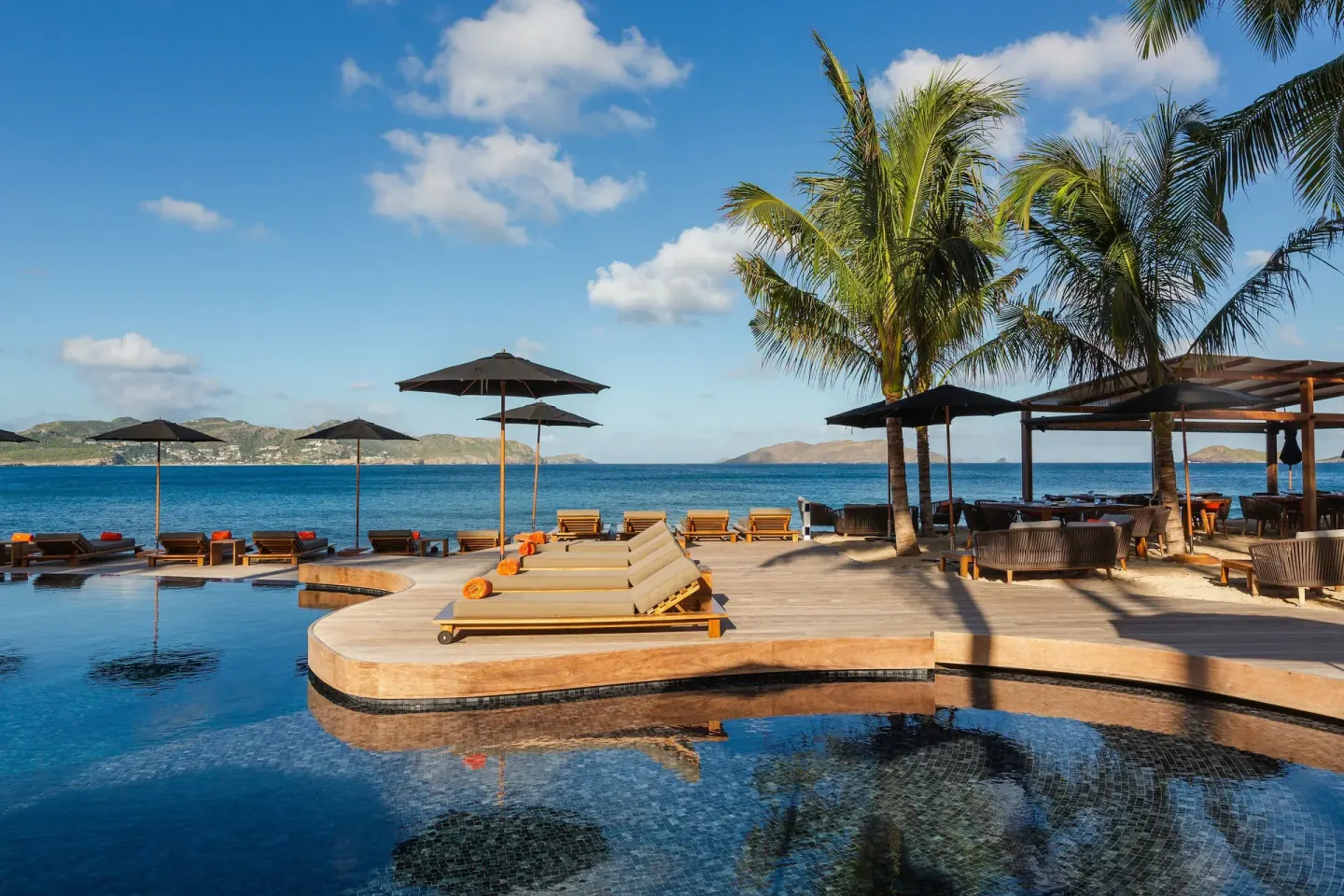 Seafront pool deck with loungers, umbrellas, and palm trees at Christopher Hotel.