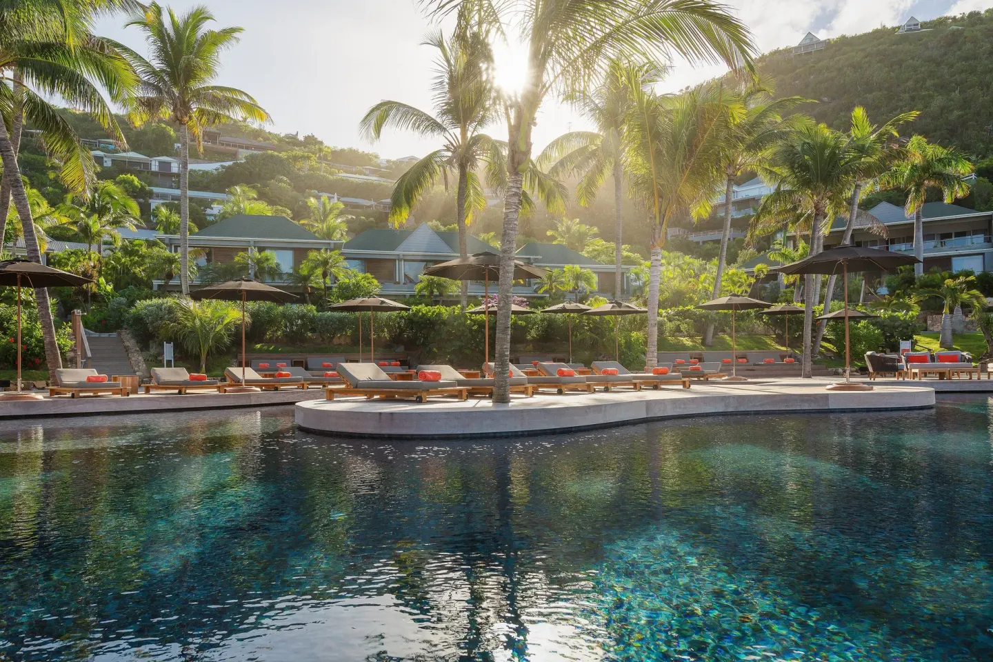 Sunlit pool area with palm trees, loungers, and hillside rooms at Christopher Hotel.
