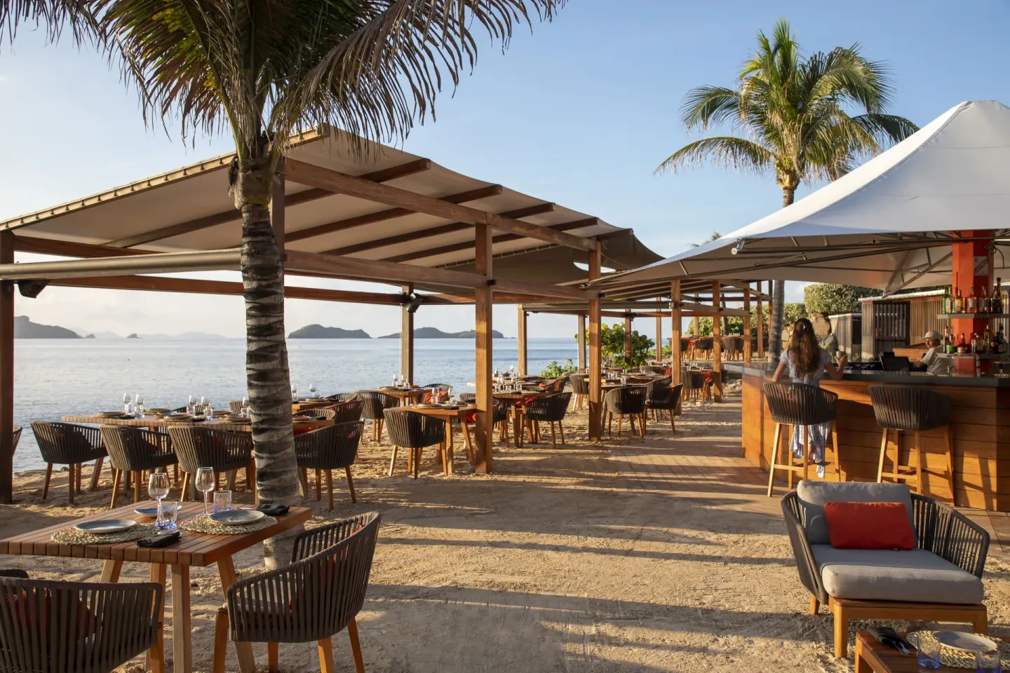 Beachfront restaurant tables and a bar sit under palms at Christopher Hotel.
