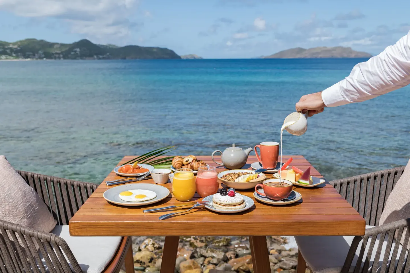 A seaside breakfast table with coffee, juice, and pastries at Christopher Hotel.