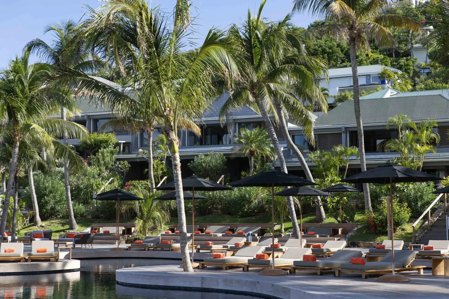 Christopher Hotel pool deck with loungers, umbrellas, palms and hillside rooms.