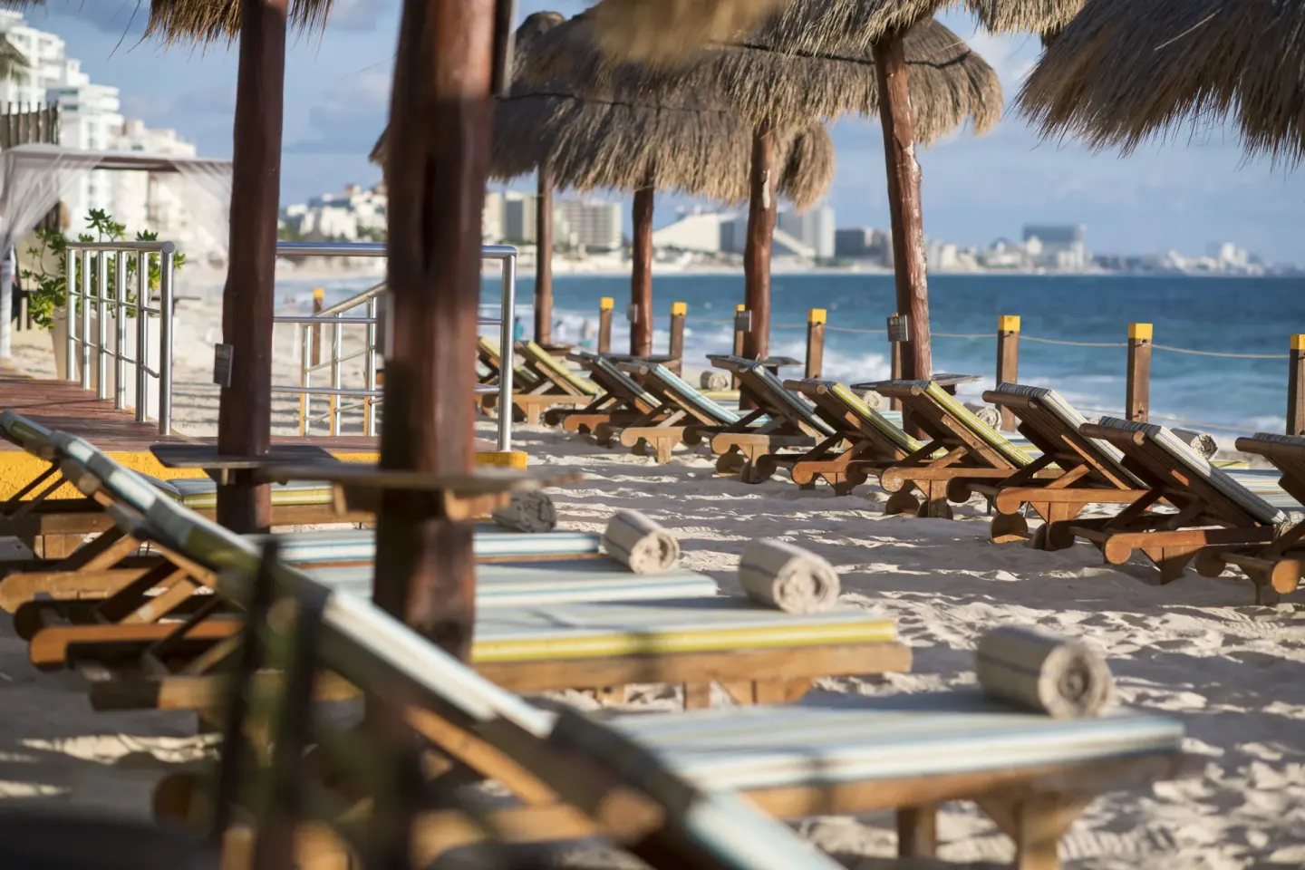Rows of beach loungers under palapas beside the water at Club Regina Cancun.
