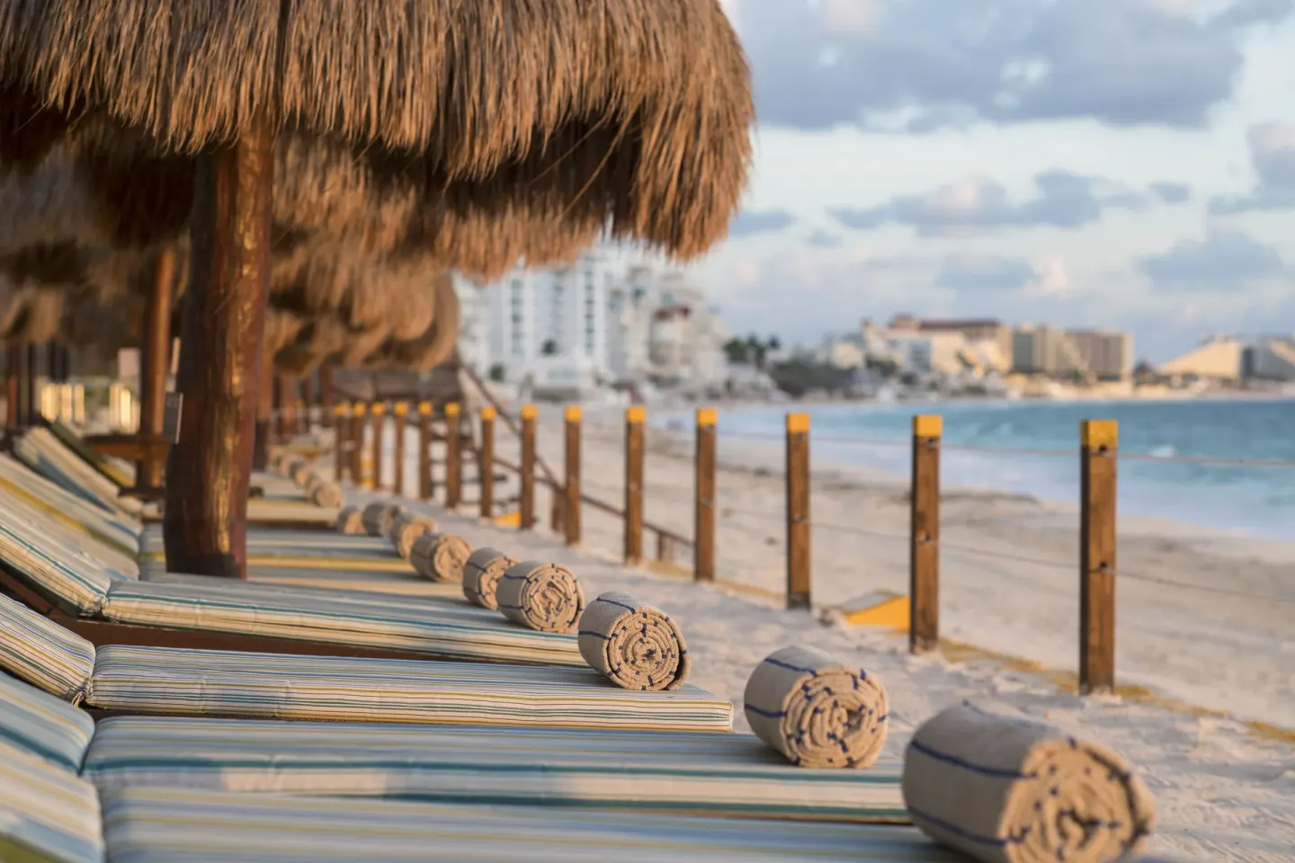 Striped beach loungers with rolled towels under palapas at Club Regina Cancun.