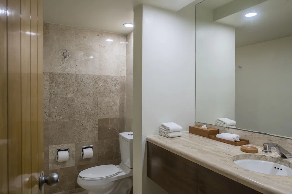 Guest bathroom with vanity, mirror, toilet, and tiled shower at Club Regina Cancun.