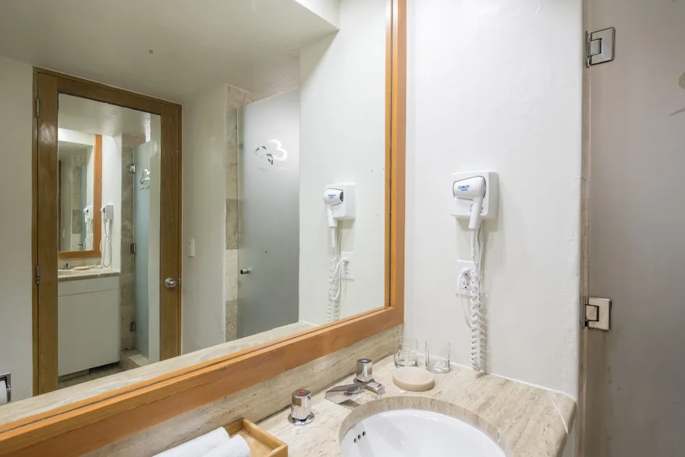 Guest bathroom sink, mirror, and wall-mounted hair dryer at Club Regina Cancun.
