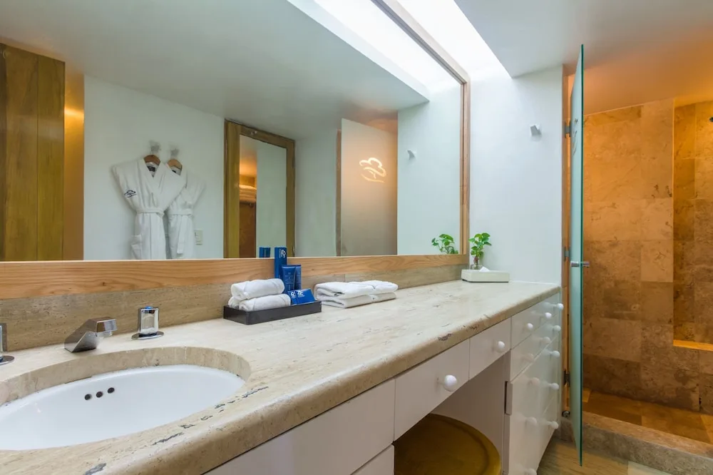 Guest bathroom with long vanity, mirror, robes and glass shower at Club Regina Cancun.