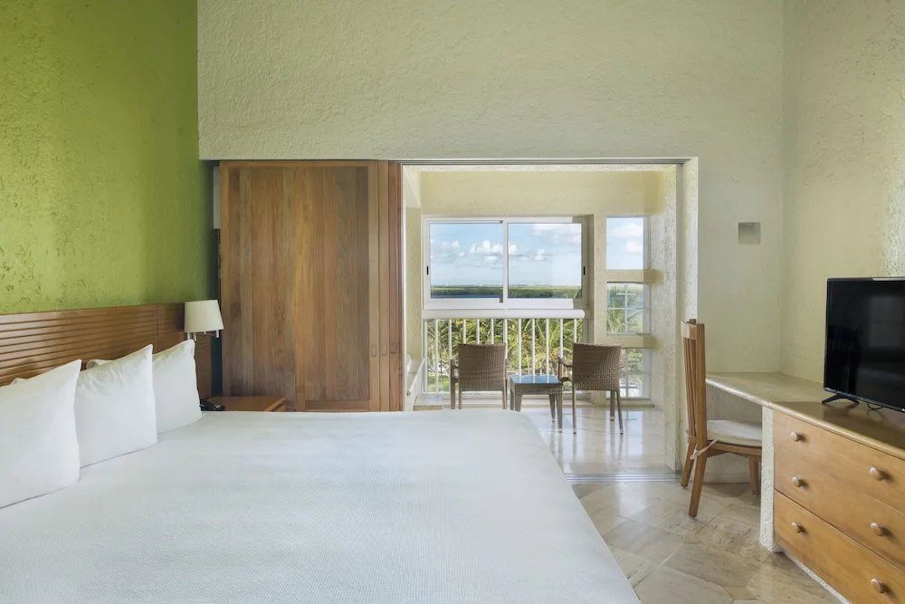 Guest room with king bed, balcony sitting area and TV at Club Regina Cancun.