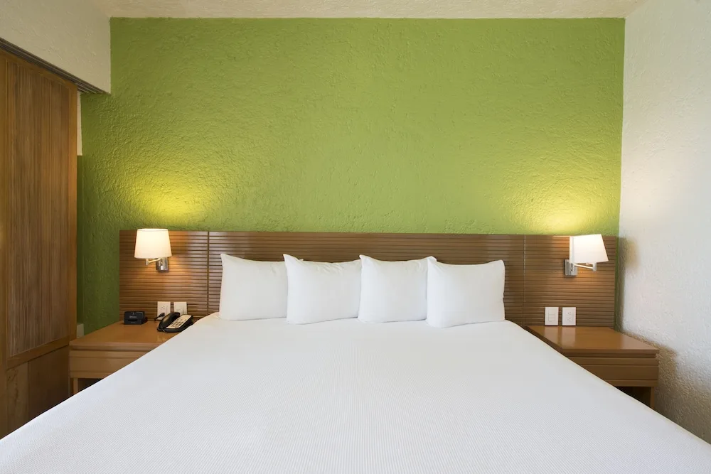 King bed with white linens and green accent wall at Club Regina Cancun.