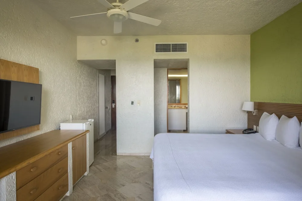 Guest room with a king bed, wall-mounted TV, and vanity area at Club Regina Cancun.