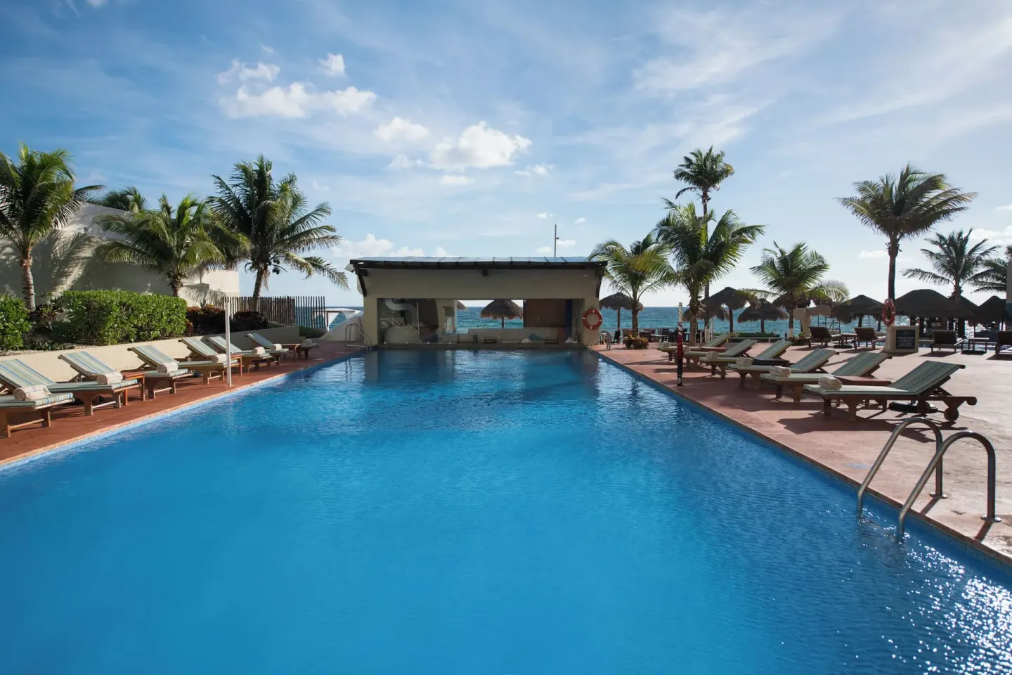 Oceanfront pool with loungers, palms, and palapa shade at Club Regina Cancun.