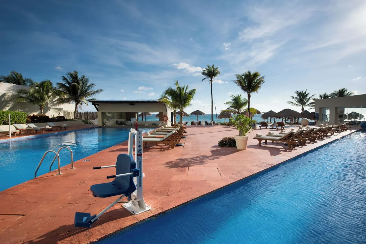 Pool deck with two pools, loungers, palms, and ocean view at Club Regina Cancun.