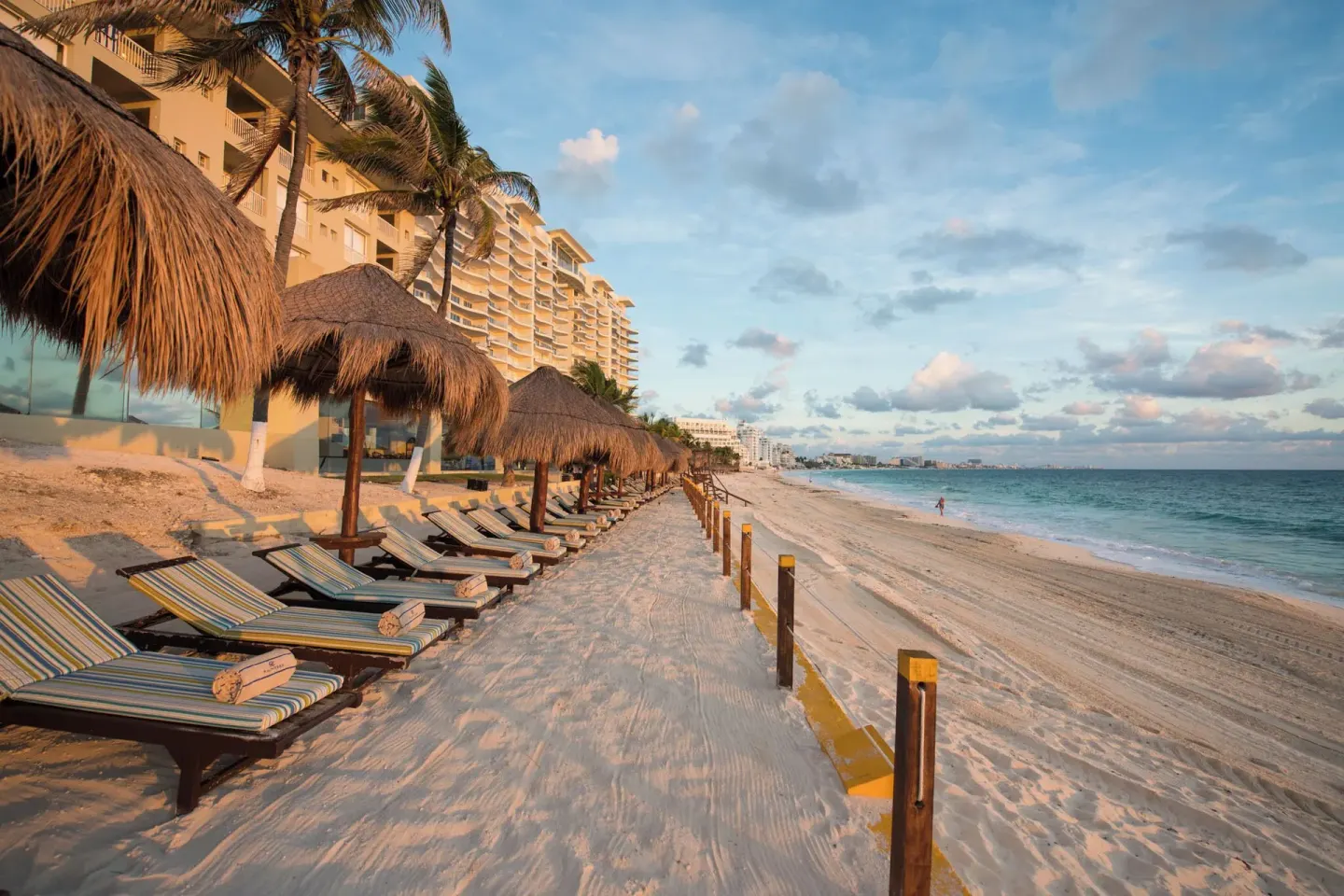 Beachfront loungers beside resort buildings and ocean at Club Regina Cancun.