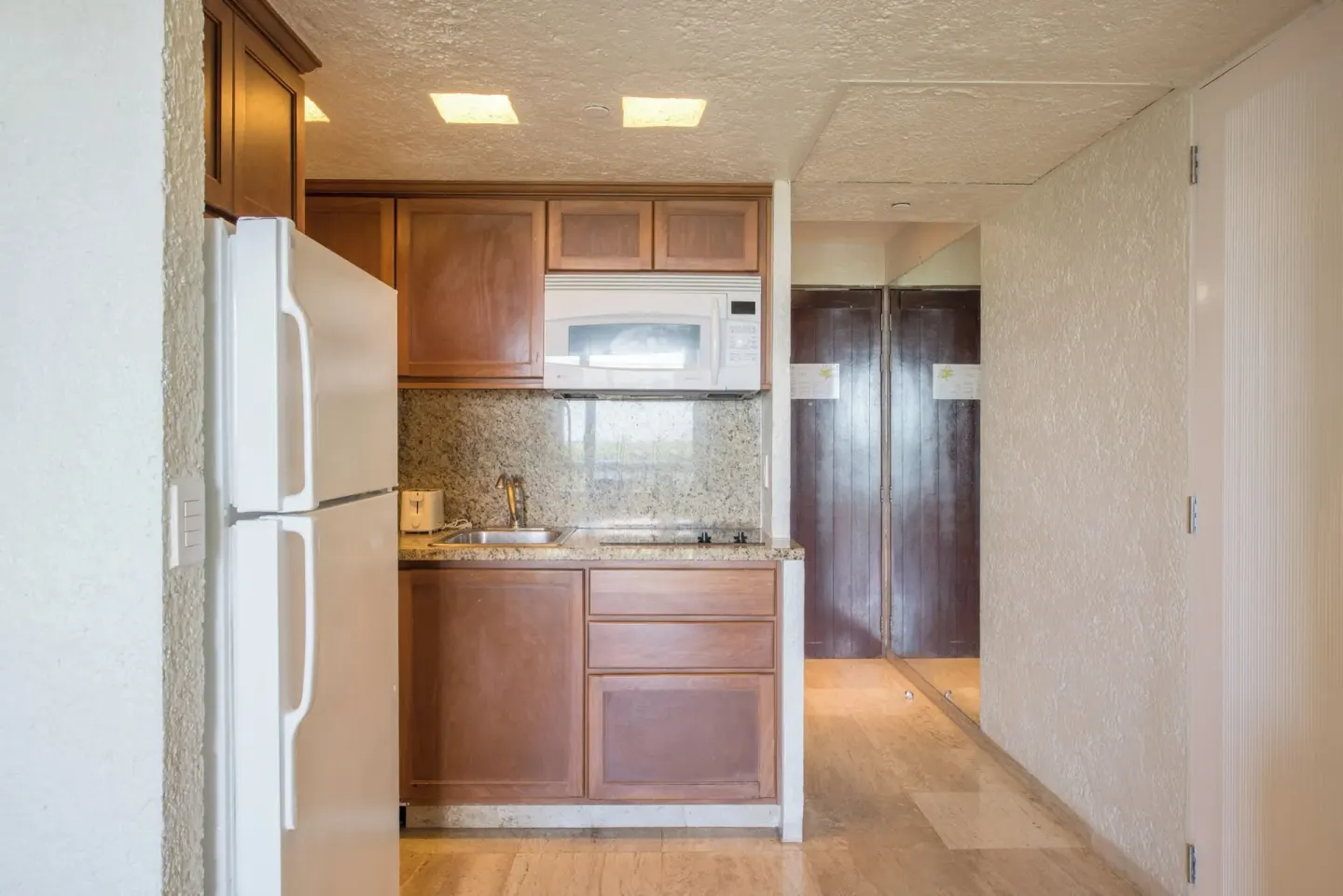 Classic Room kitchenette with refrigerator and wood cabinets at Club Regina Cancun.