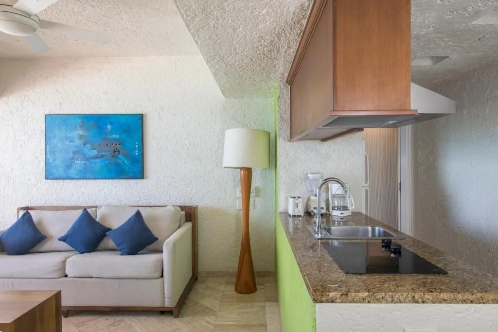 Deluxe Suite living area and kitchenette at Club Regina Cancun with sofa and granite counter.