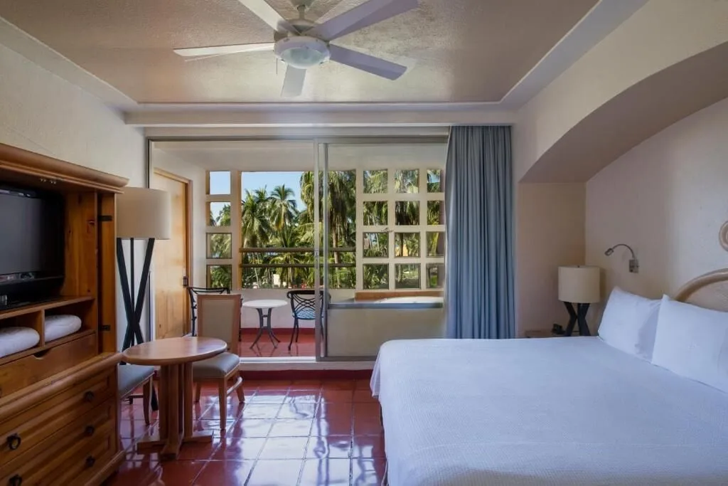King bed guest room with balcony and palm views at Club Regina Puerto Vallarta.