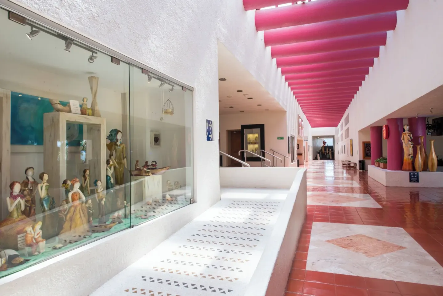 Indoor corridor with display cases and red ceiling beams at Club Regina Puerto Vallarta.