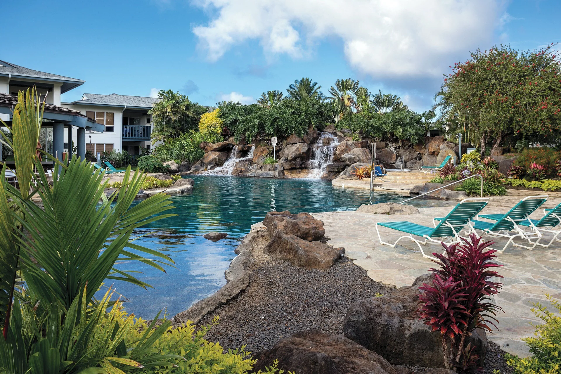 Poolside lounge chairs beside a rock waterfall and tropical plants at Club Wyndham Bali Hai Villas.
