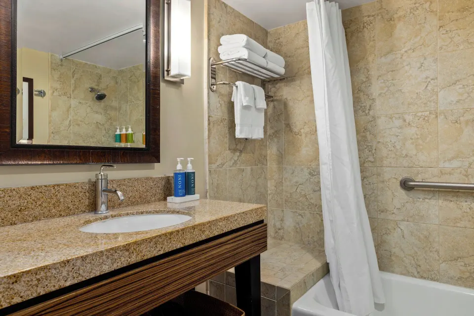 Standard Studio bathroom with vanity, tub, shower curtain, and towels at Club Wyndham Royal Garden at Waikiki.